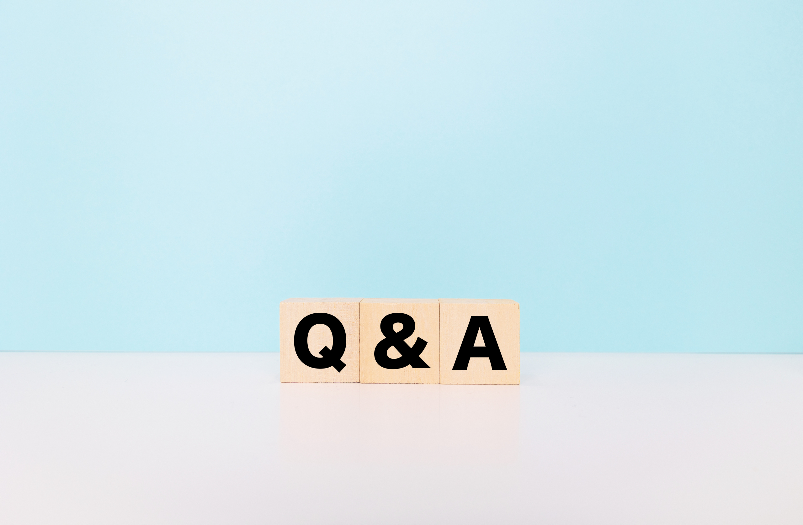 水色の背景の白いテーブルに置かれた木製のブロックで「Q & A」と書かれている。質疑応答、疑問解決、サポートのイメージ。