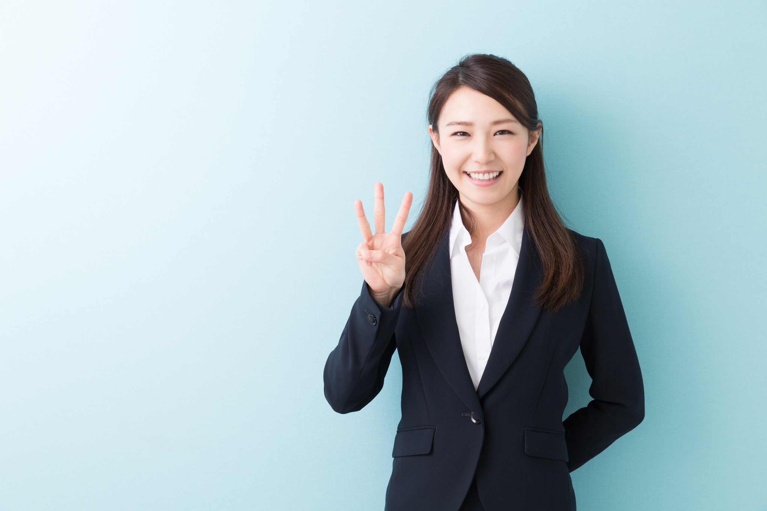 スーツ姿で笑顔の日本人女性が、指で数字の『3』を示しています。